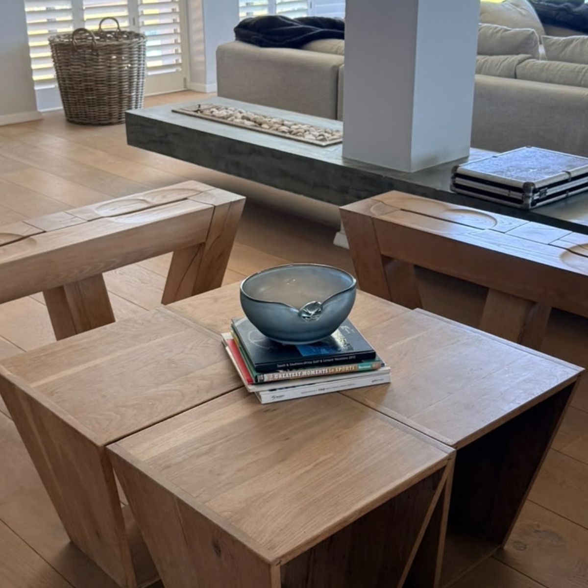 Pebble Dusk Bowl on a stack of books on a wooden coffee table in a living room — low sculptural smoky glass bowl, HMT Home